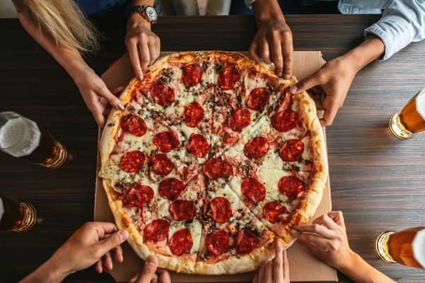 Hands reaching for a large pepperoni pizza on a table, perfect for a fun and satisfying experience on the Vegas Pot & Pizza Tour by 420 Party Tours.